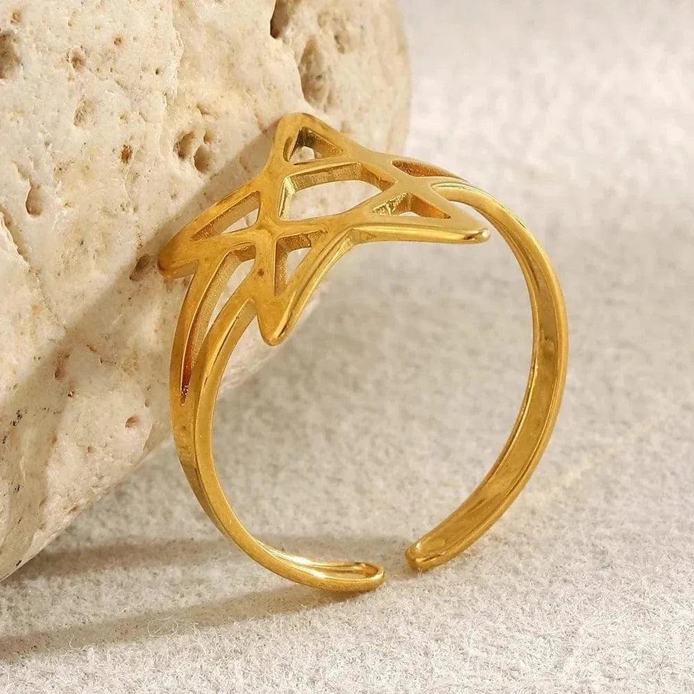 Gold ring with a star design on a textured beige surface