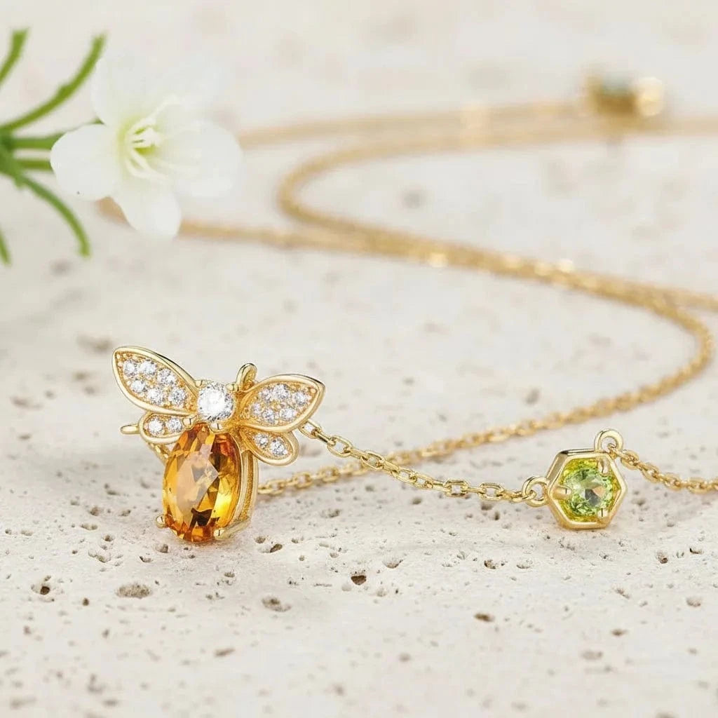 Gold necklace with bee pendant and yellow gemstone on a light background.
