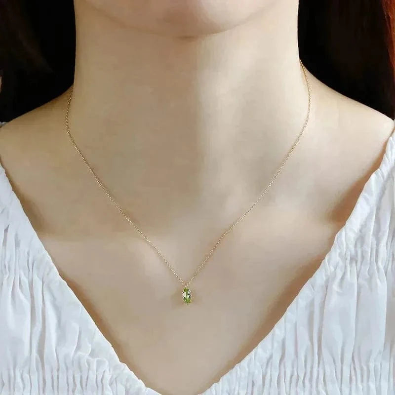 Gold necklace with a green pendant on a mannequin wearing a white top.