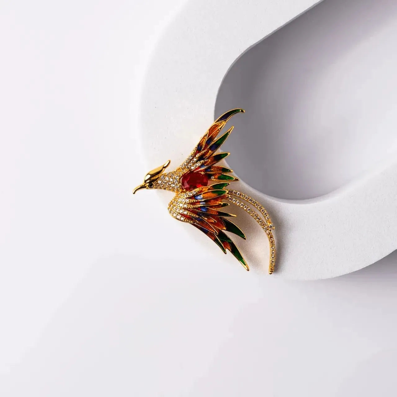 Gold red phoenix pin with green gemstones on a white background