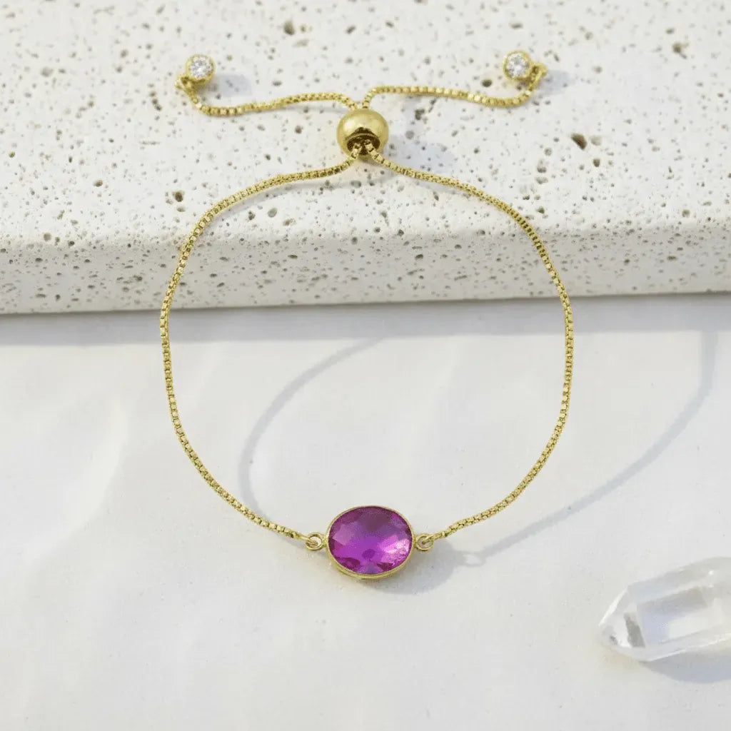 Gold bracelet with a purple gemstone on a textured surface
