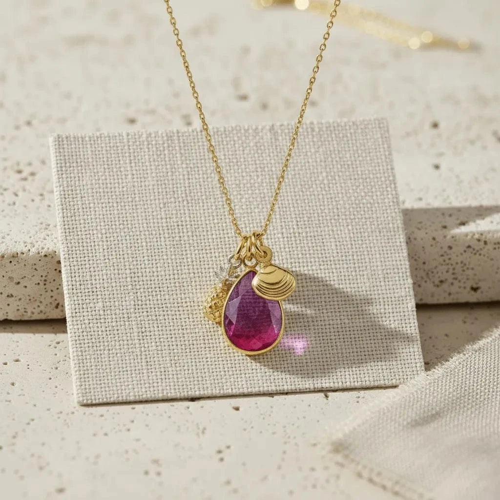 Gold necklace with a purple teardrop pendant on a textured surface