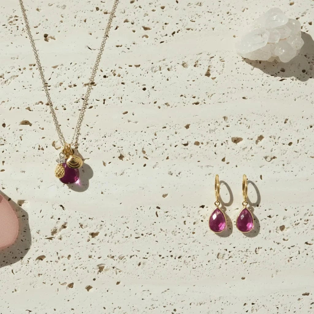 Gold necklace and earrings with pink gemstones on a textured beige surface