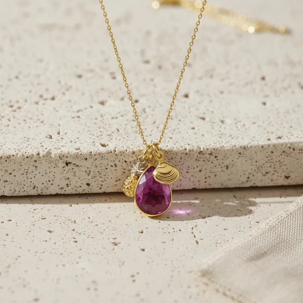 Gold necklace with a purple teardrop pendant on a textured surface