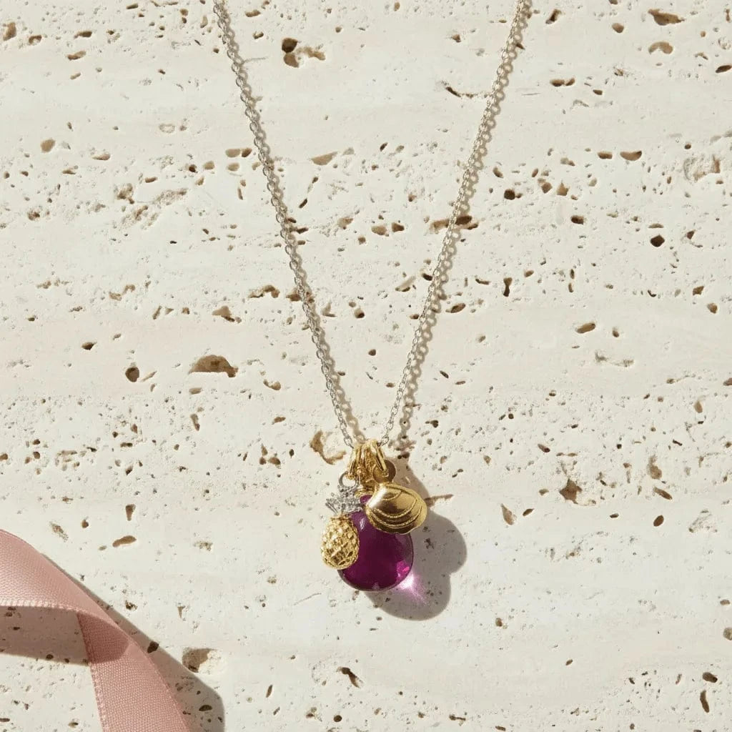 Necklace with a purple teardrop pendant and gold accents on a textured beige surface.