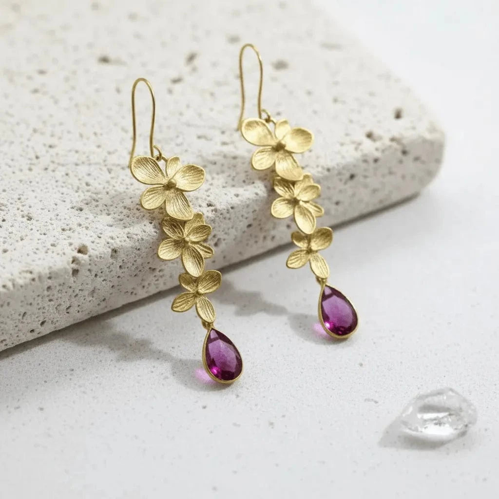 Gold floral earrings with purple teardrop accents on a white background