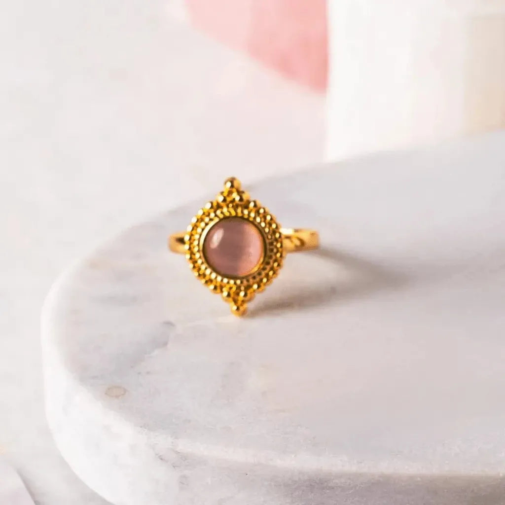 Gold ring with a pink gemstone on a marble surface