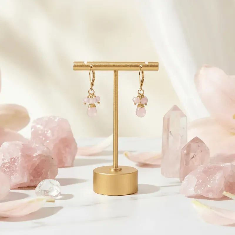 Gold earring stand with pink earrings surrounded by pink crystals on a soft beige background