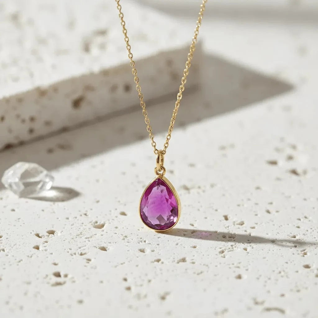 Gold necklace with a pink teardrop pendant on a textured surface