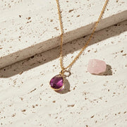 Gold necklace with a purple gemstone pendant on a light stone surface