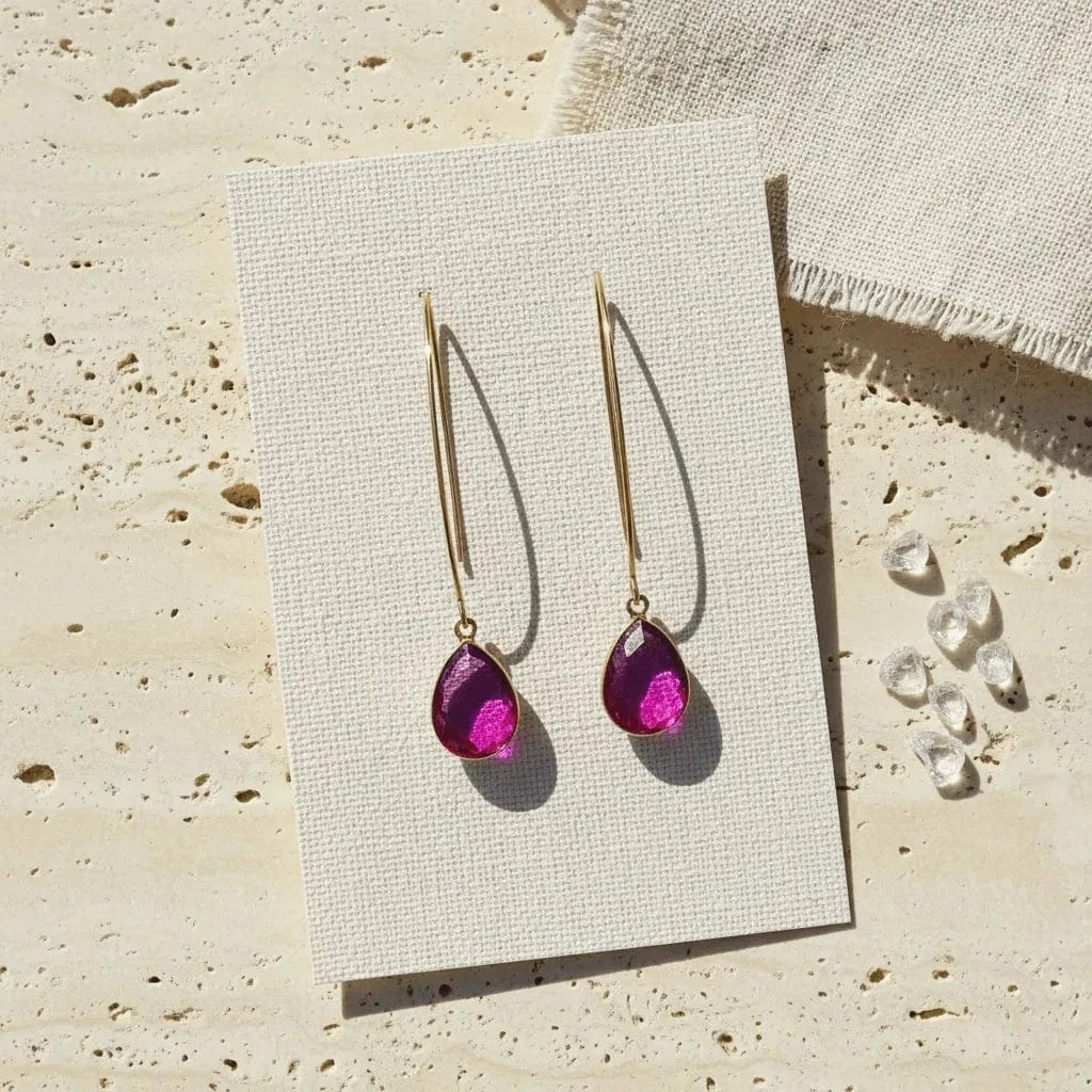 Gold earrings with purple teardrop stones on a textured beige surface