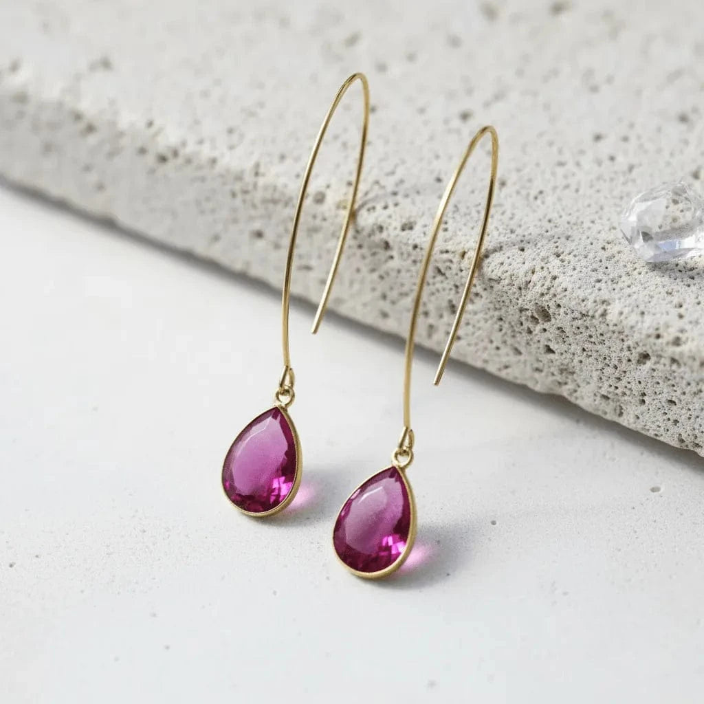 Gold earrings with pink teardrop-shaped gemstones on a light background