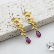 Gold floral earrings with purple teardrop charms on a textured surface