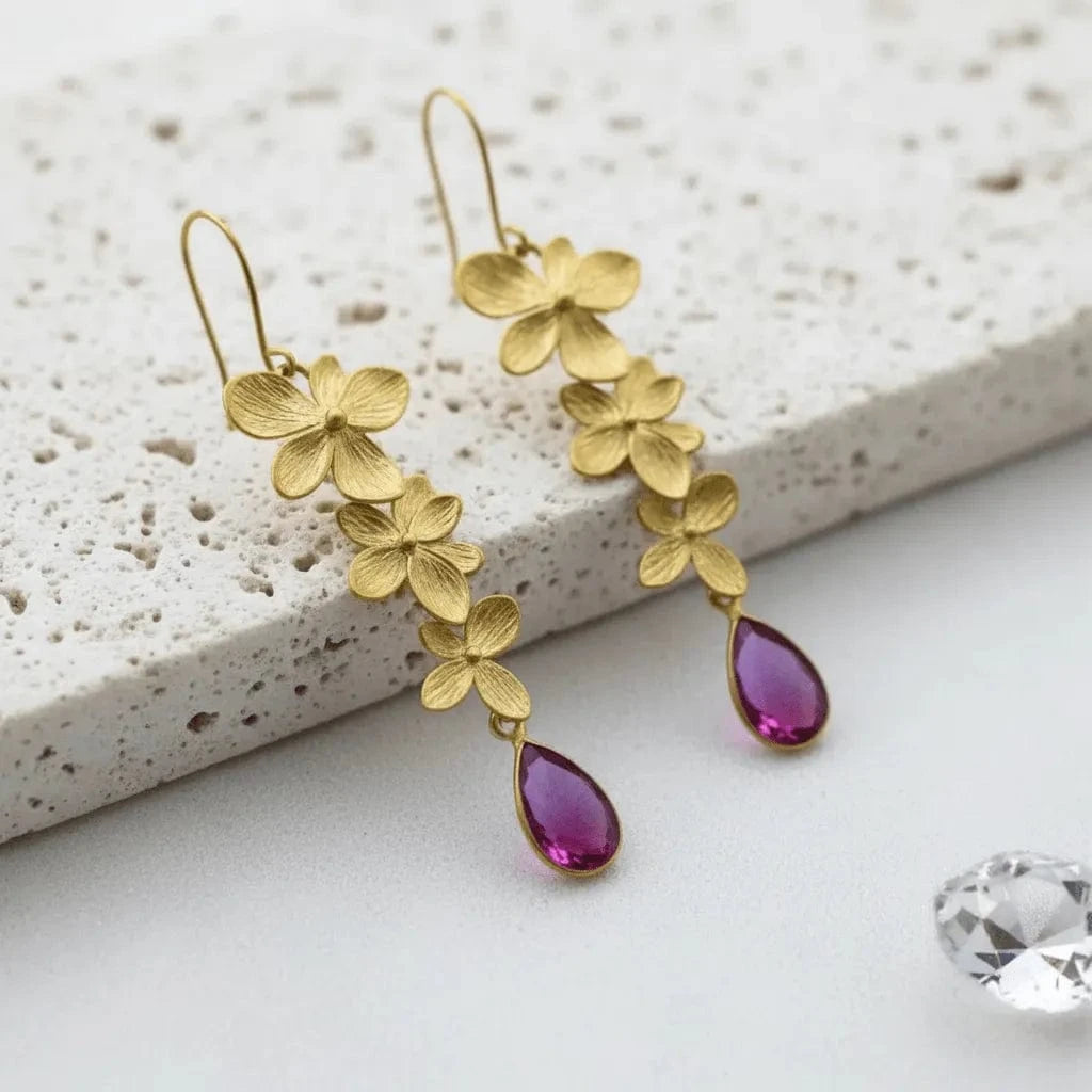 Gold floral earrings with purple teardrop charms on a textured surface