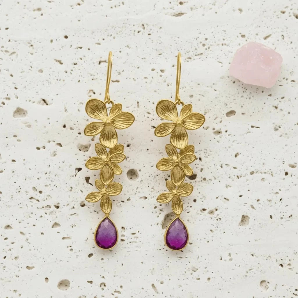 Gold floral earrings with purple drops on a textured surface