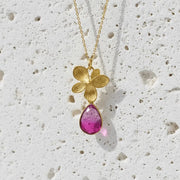 Gold necklace with a pink teardrop pendant on a textured white background