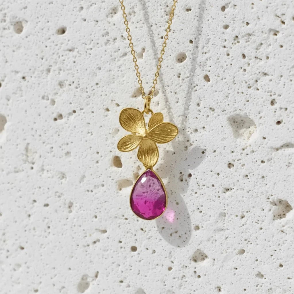 Gold necklace with a pink teardrop pendant on a textured white background