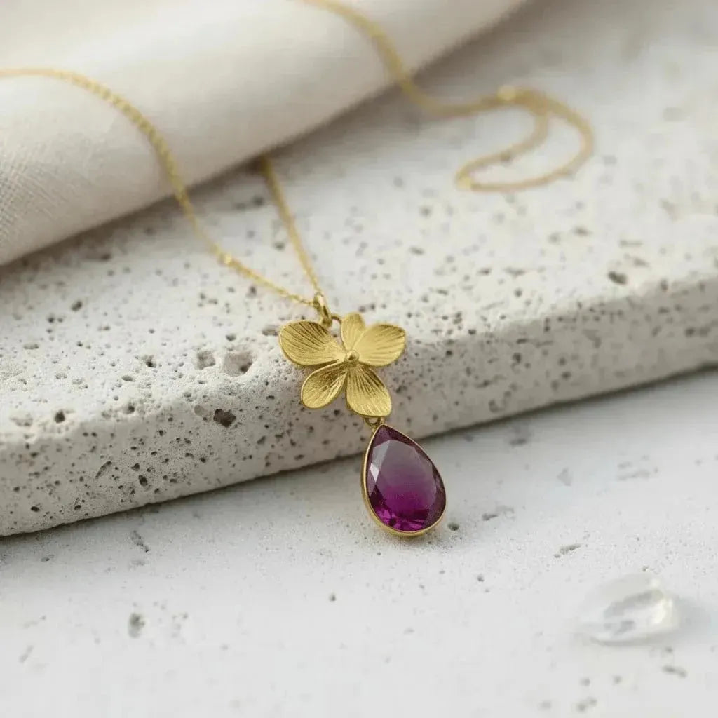 Gold necklace with a pink teardrop pendant on a textured white background