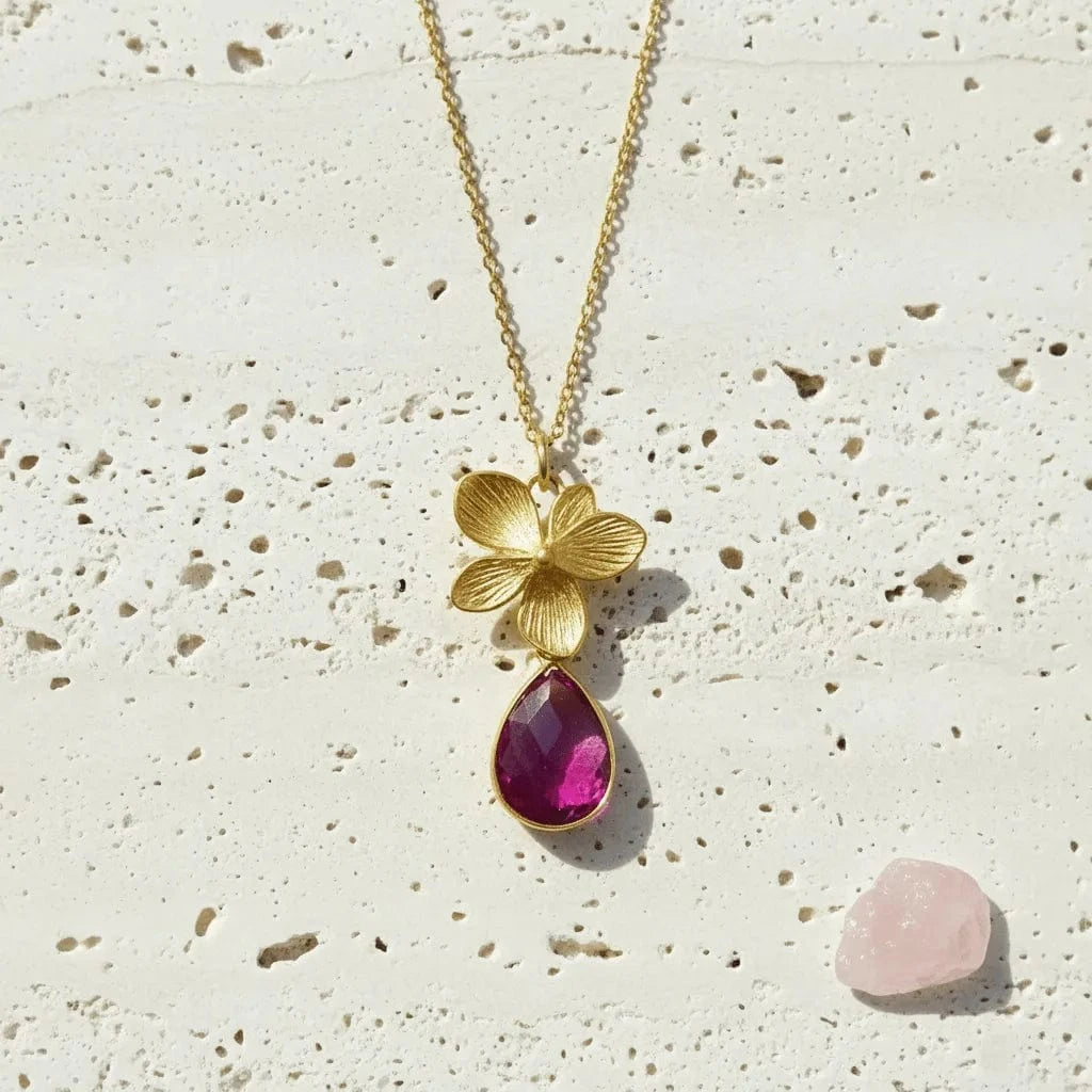 Gold necklace with a pink teardrop pendant on a textured beige surface