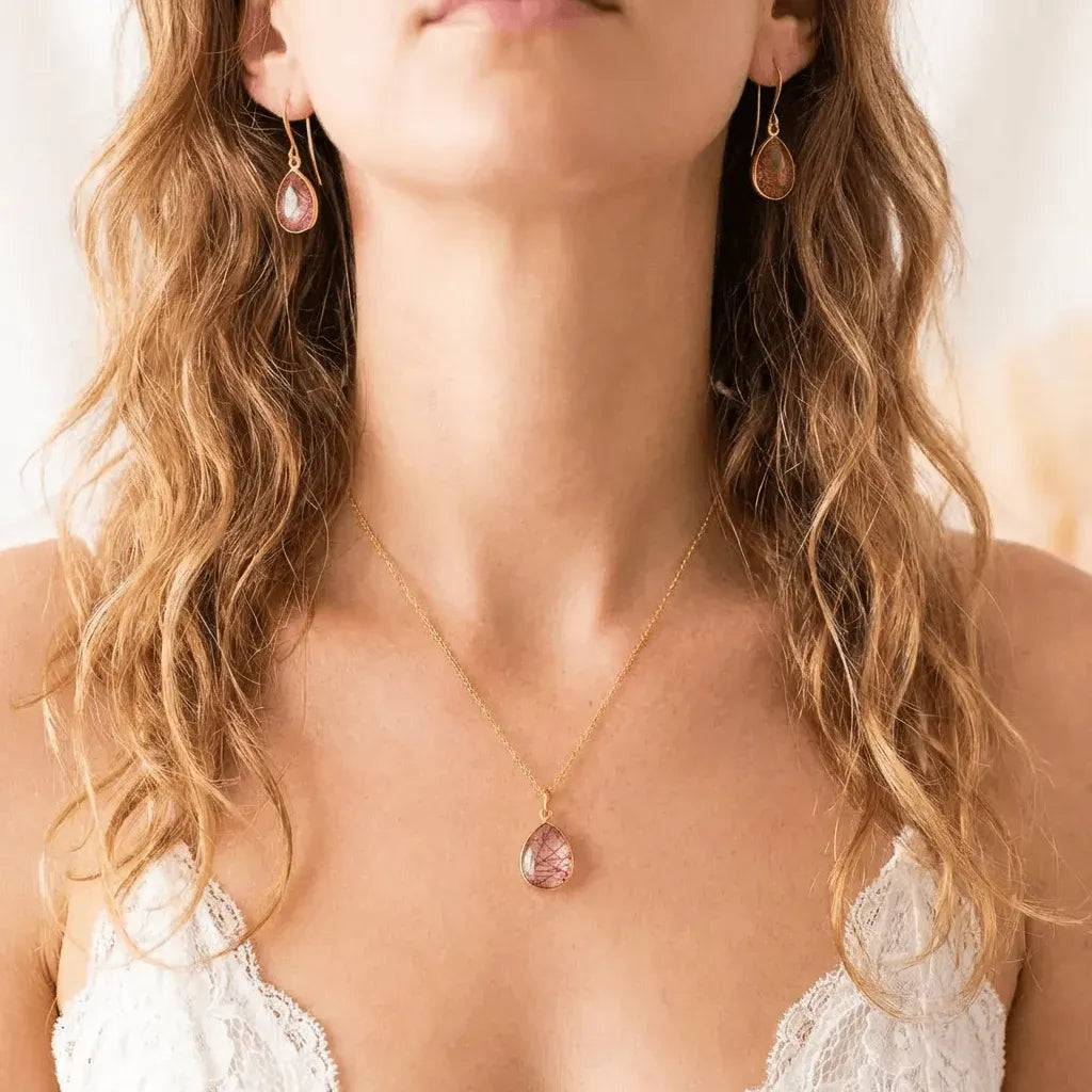 Woman wearing a gold necklace with a pink pendant and matching earrings.