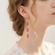 Woman wearing pink rutilated quartz triple-link earrings in gold — 58mm cascade drop