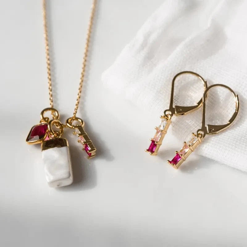 Gold necklace with a pearl pendant and red gemstones, paired with matching earrings on a white background.