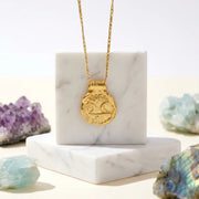 Gold necklace with a pendant on a marble stand surrounded by crystals