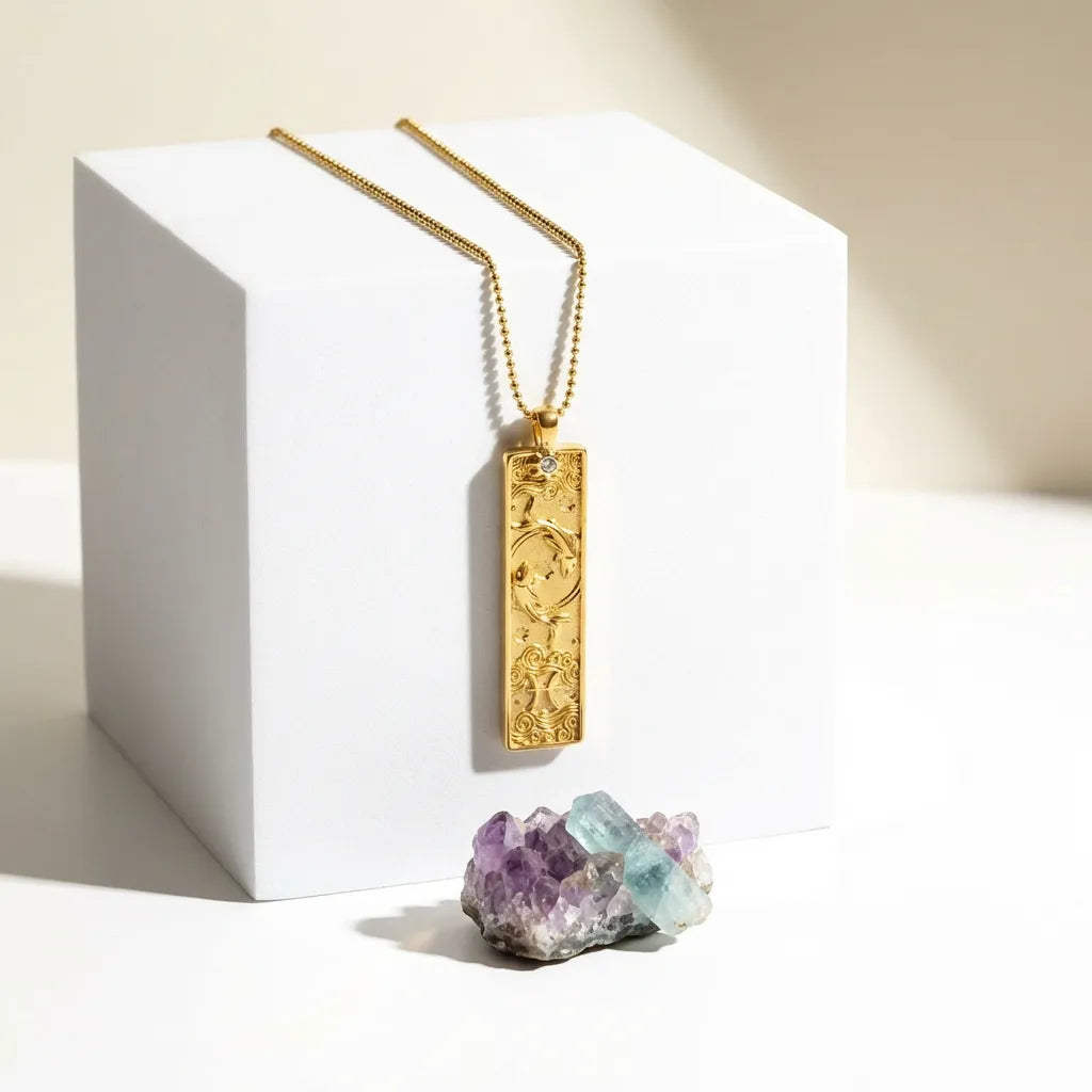 Gold necklace with a pendant on a white cube, next to amethyst and aquamarine crystals.