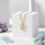 Gold necklace with a pendant on a white block, surrounded by crystals