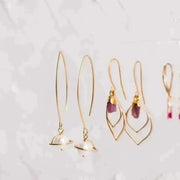 Gold earrings with pink gemstones on a light gray background