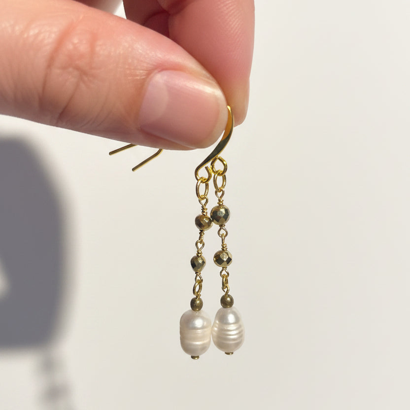 Gold potato pearl and pyrite drop earrings held in hand to show scale