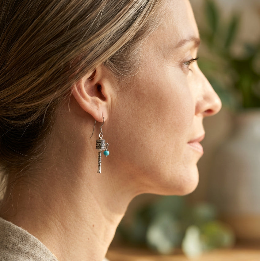 Woman wearing silver-plated Tibetan prayer wheel drop earrings with turquoise blue beads