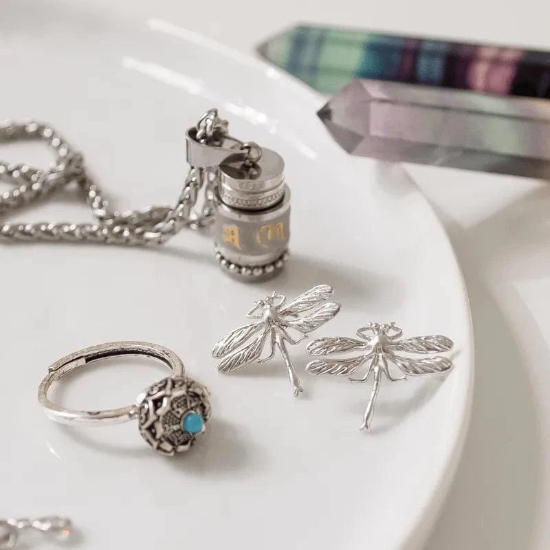 Silver jewelry including a necklace, ring, and dragonfly earrings on a white surface with a crystal in the background.