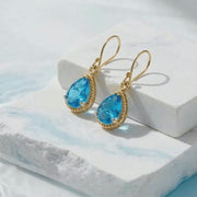 white stone background with water and vivid blue gold earrings