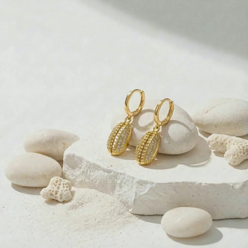 cowrie shell earrings with water on beach