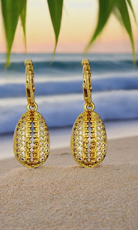 Gold cowrie shell earrings with crystals on a beach background, adding a touch of ocean elegance.