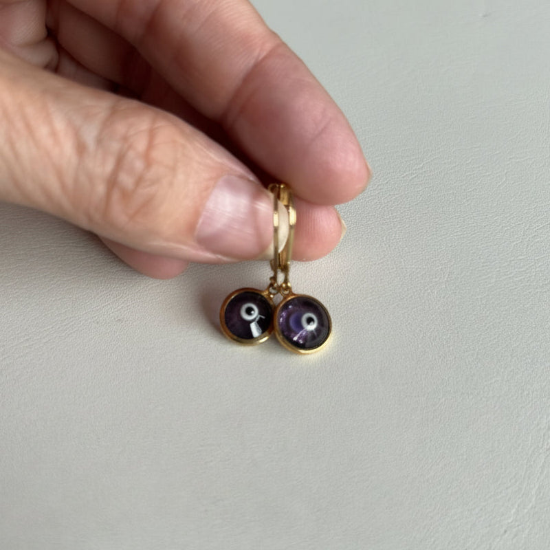 Purple mini evil eye earrings held in hand, protection symbol jewelry