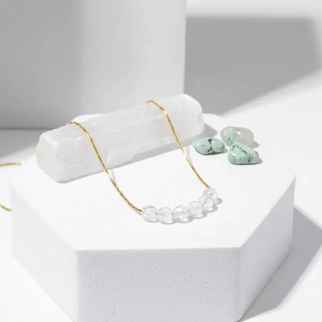 Necklace with gold chain and clear beads on a white stand, accompanied by green earrings.