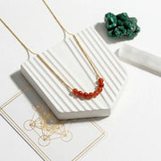 Necklace with red beads on a white surface with a green stone in the background