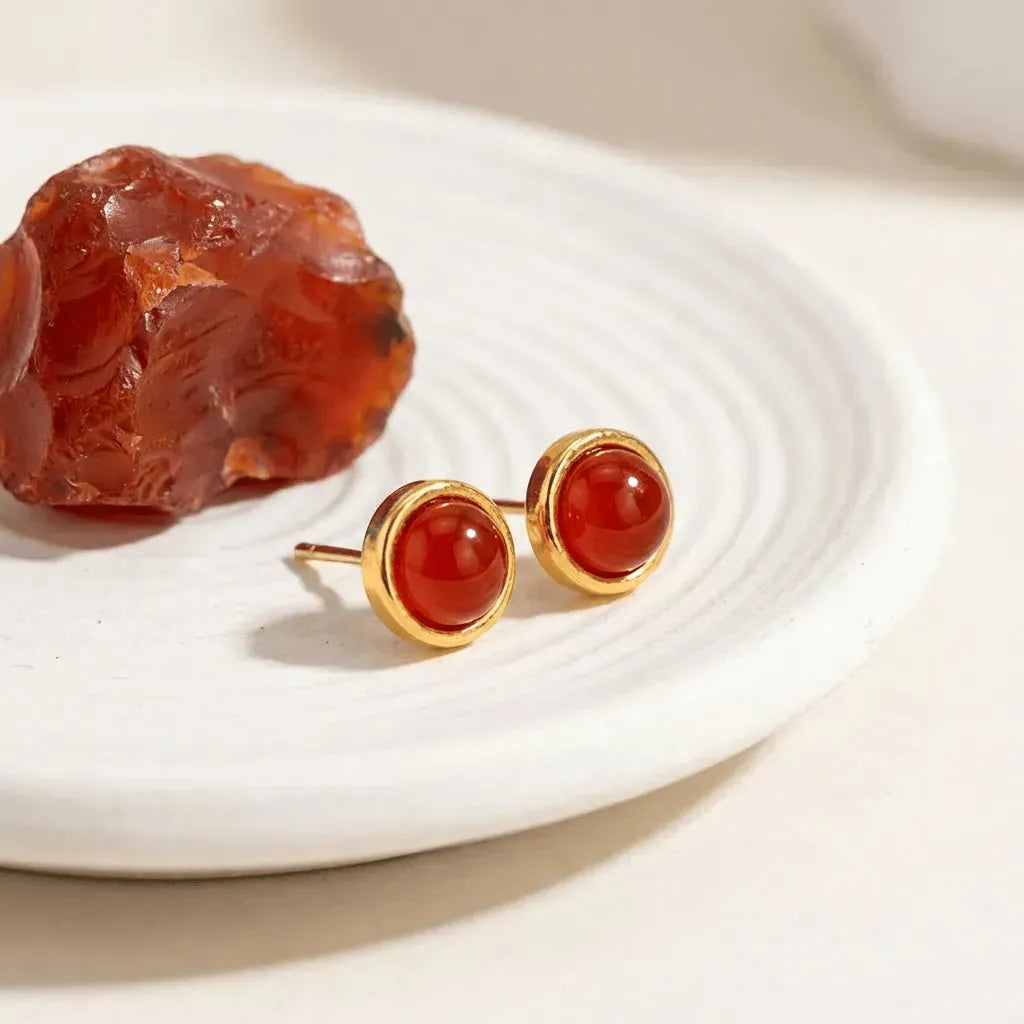 Gold earrings with red stones on a white plate with a piece of amber.
