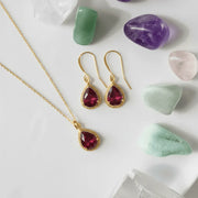 Gold jewelry set with red gemstones on a white surface with stones