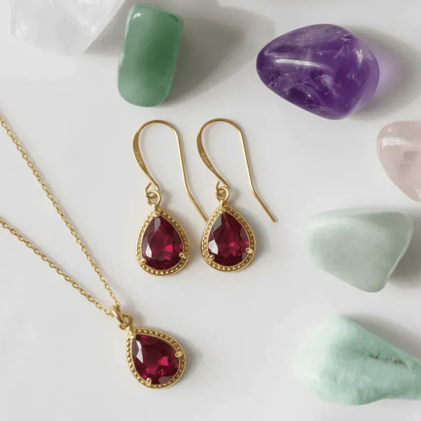 Gold jewelry set with red gemstones on a white surface with stones.