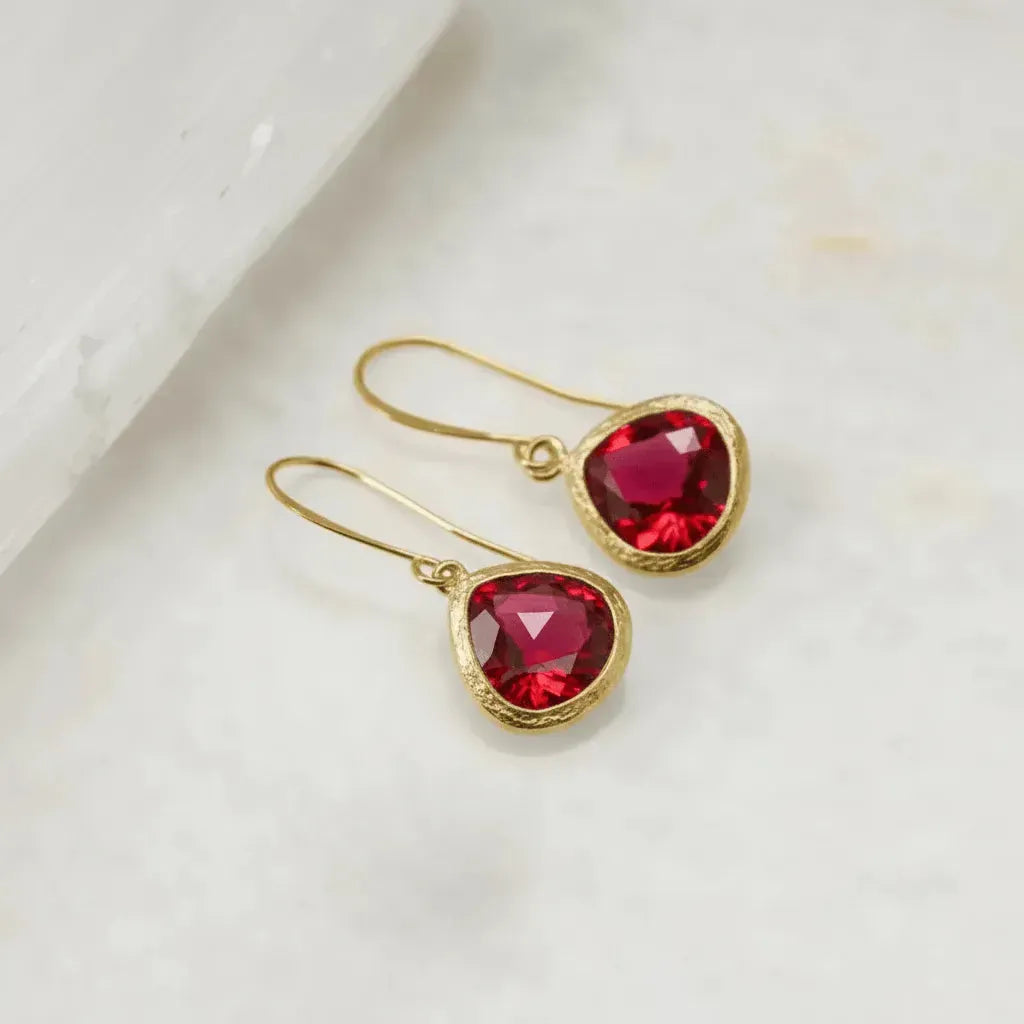 Gold earrings with red gemstones on a white surface