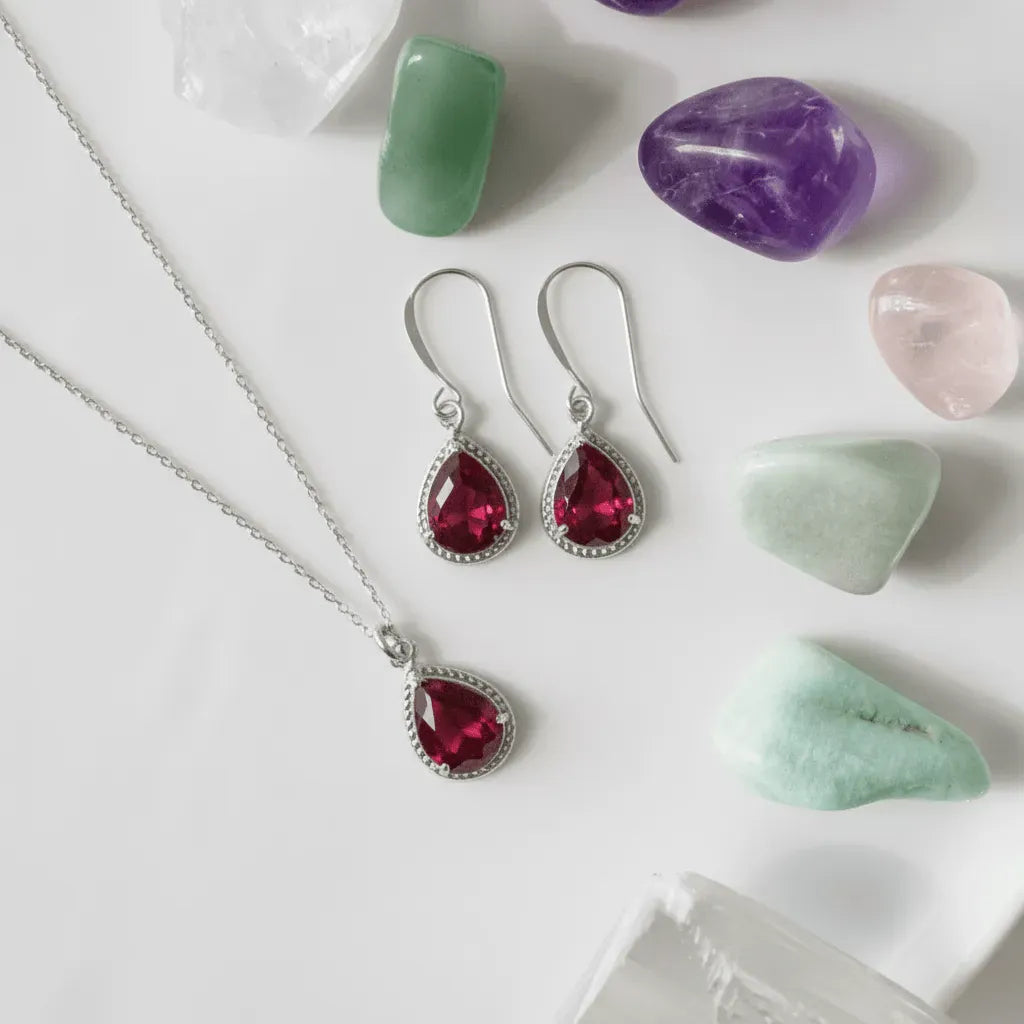 Silver jewelry set with red gemstones on a white surface with stones.