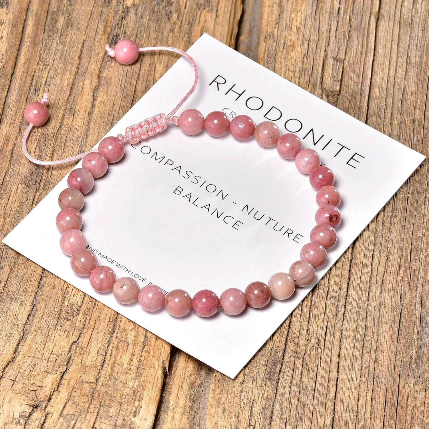 Pink rhodonite bracelet on a card with text on a wooden surface