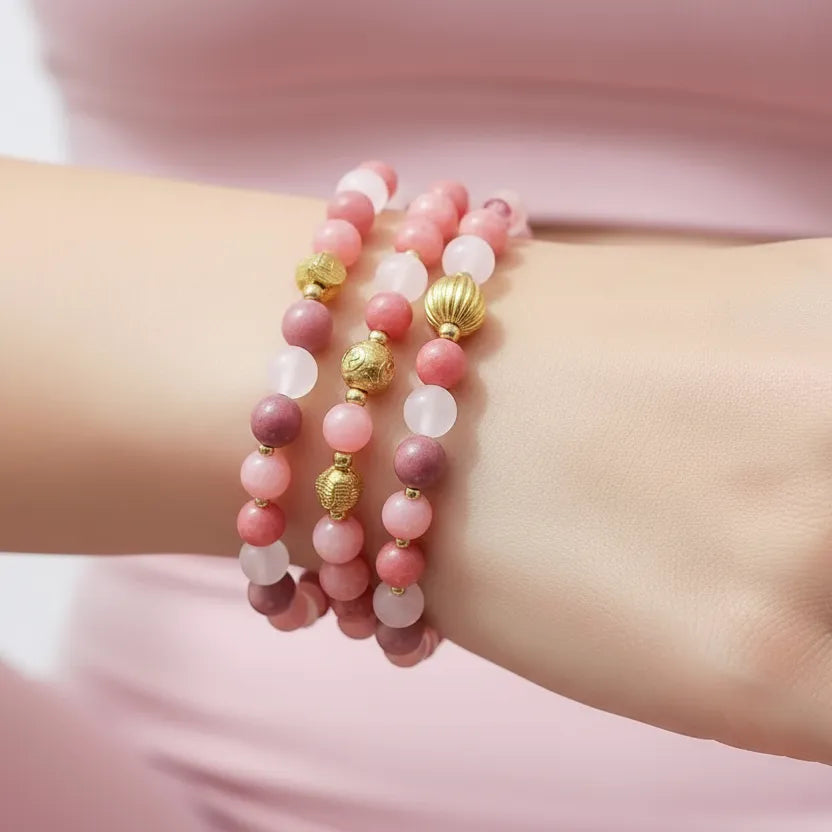 Stack of pink and gold beaded bracelets on a wrist with a soft pink background