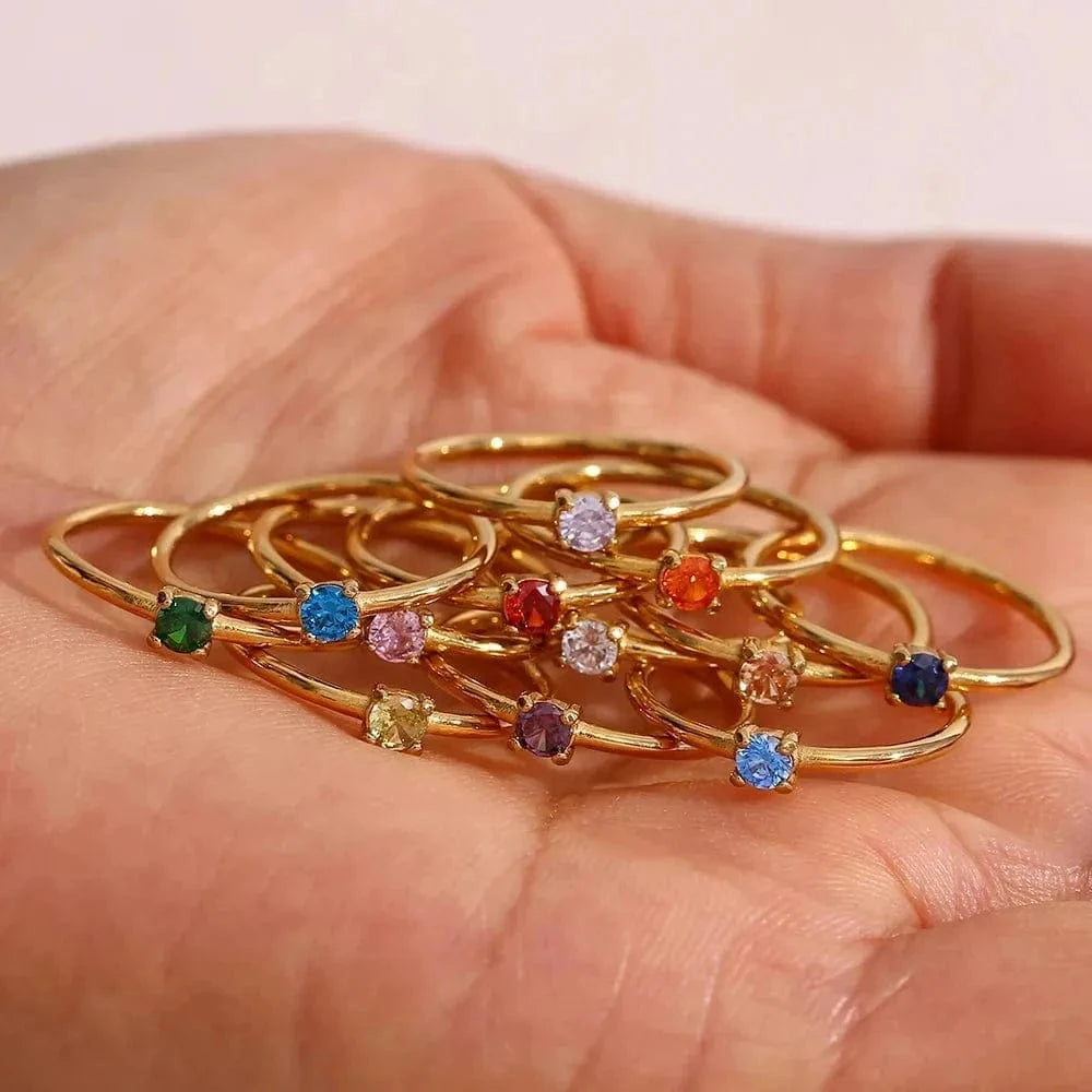 Gold rings with colorful gemstones held in a hand against a neutral background