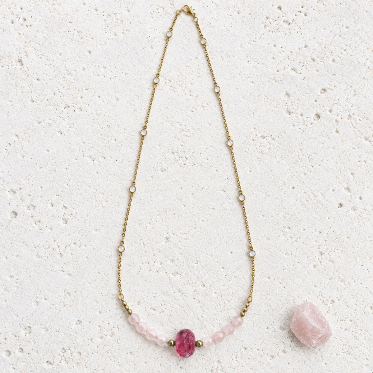 Full length of the rose quartz and moonstone necklace laid flat, showing the moonstone station chain and pink glass focal beside raw rose quartz
