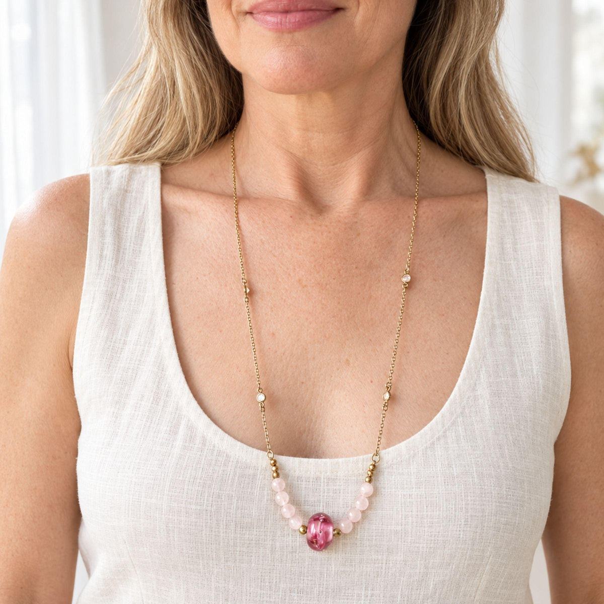 Rose quartz and moonstone necklace worn over a white tank top, pink glass focal resting well below the collarbone