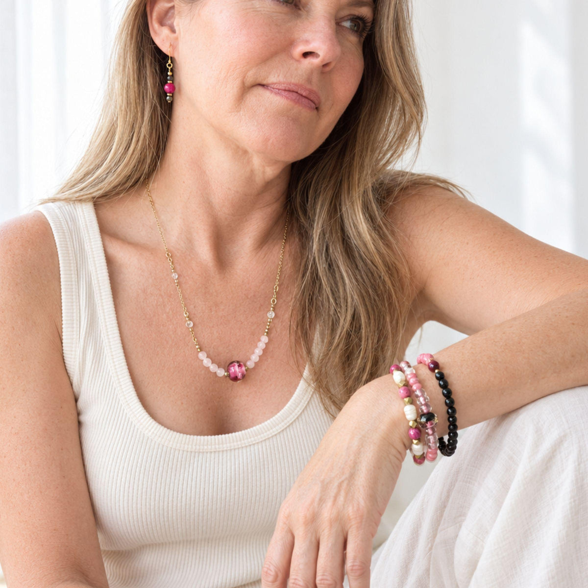 Woman wearing the rose quartz and moonstone necklace with a stack of pink beaded bracelets, including the rose quartz stretch bracelet